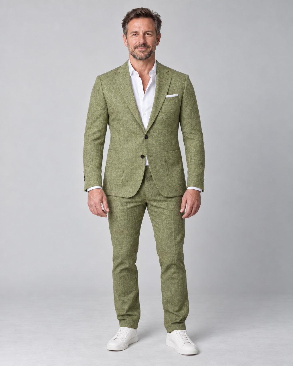 Man in groen pak met wit overhemd en witte sneakers, volledig van voren in beeld.