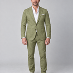 Man in groen pak met wit overhemd en witte sneakers, volledig van voren in beeld.
